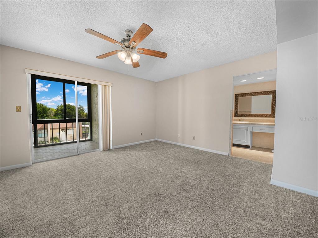 A carpeted bedroom features a ceiling fan, sliding glass doors to a balcony, and an ensuite — 1130 N LAKE PARKER AVENUE UNIT A308, LAKELAND, FL