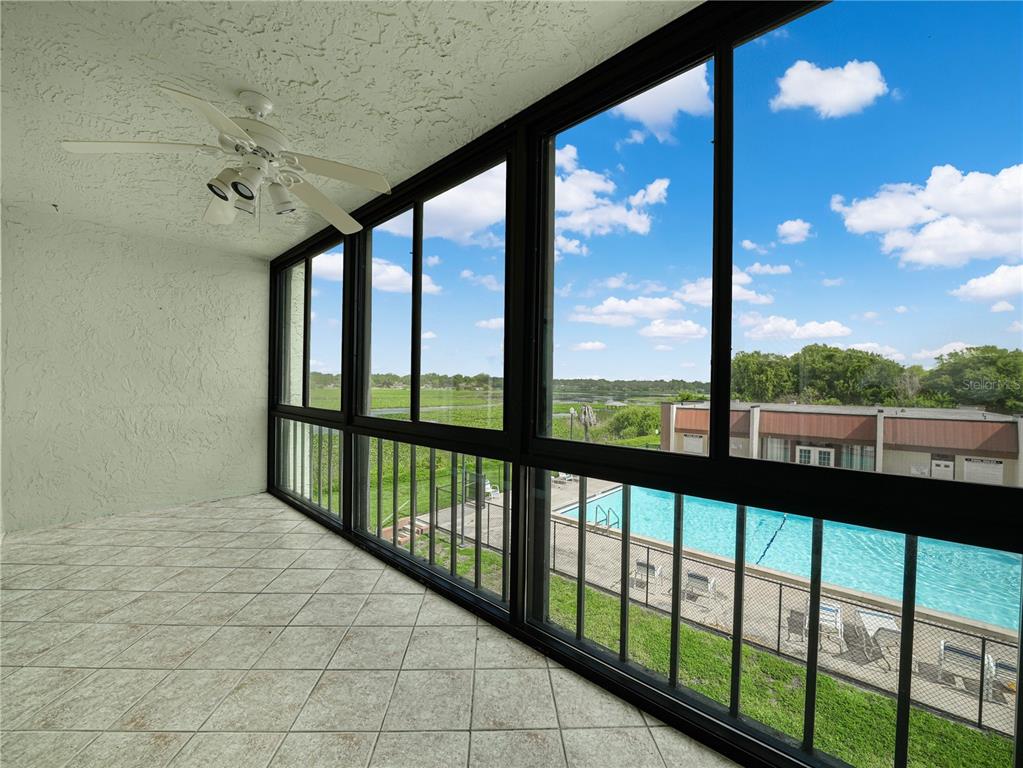A tiled balcony with a ceiling fan overlooks a swimming pool and a grassy field — 1130 N LAKE PARKER AVENUE UNIT A308, LAKELAND, FL