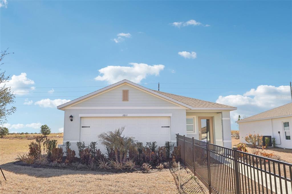 A light-colored single-story house with a two-car garage and a black metal fence — 5331 CLOUDBERRY AVENUE, LAKELAND, FL