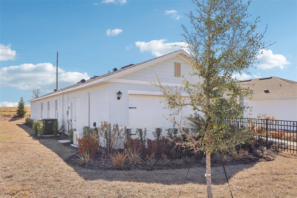 A side view of a white house exterior with a garage and landscaped yard — 5331 CLOUDBERRY AVENUE, LAKELAND, FL