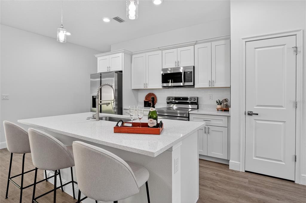 A modern kitchen features white cabinetry, stainless steel appliances, and a quartz-topped island with seating — 99 W GOLDCOAST PLACE, DUNNELLON, FL