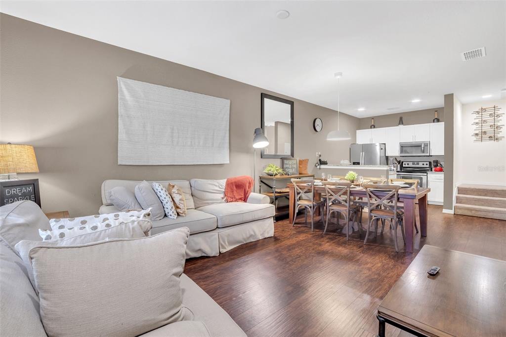 An open-concept living and dining area features hardwood floors, a white sofa, and kitchen cabinetry — 8932 SHINE DRIVE, KISSIMMEE, FL