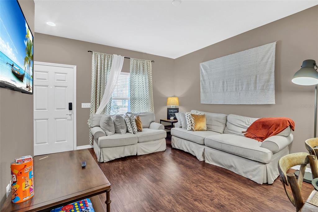 A living room features light-colored sofas, wood-look flooring, and a wall-mounted television — 8932 SHINE DRIVE, KISSIMMEE, FL