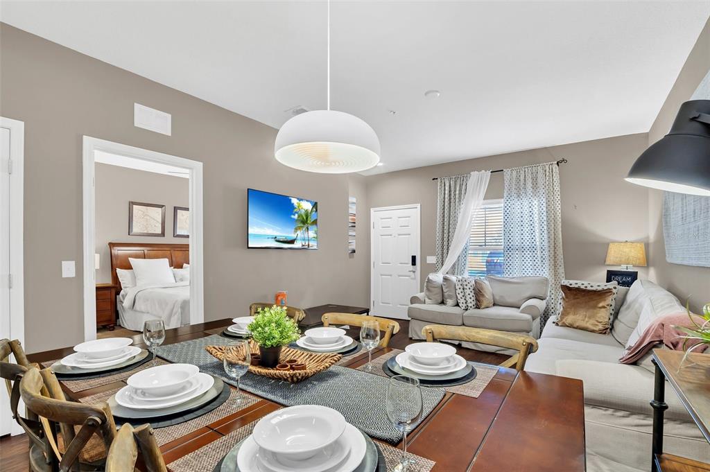 A dining area with a wooden table leads into a living room and bedroom — 8932 SHINE DRIVE, KISSIMMEE, FL