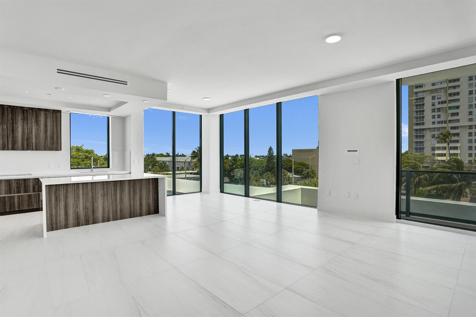 A modern kitchen with wood-toned cabinetry and a white island overlooks a bright living area — 305 Briny Avenue # 306, Pompano Beach FL 33062, POMPANO BEACH, FL
