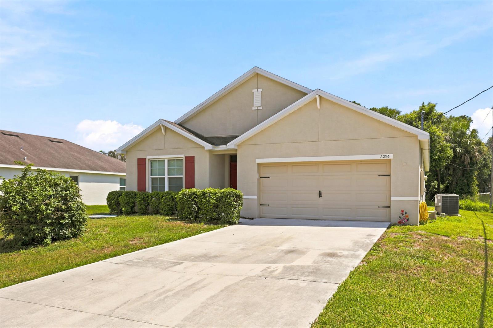 A single-story house with a beige stucco exterior, a two-car garage, and red window shutters — 2096 SW Leafy Road, FL 34953, FL