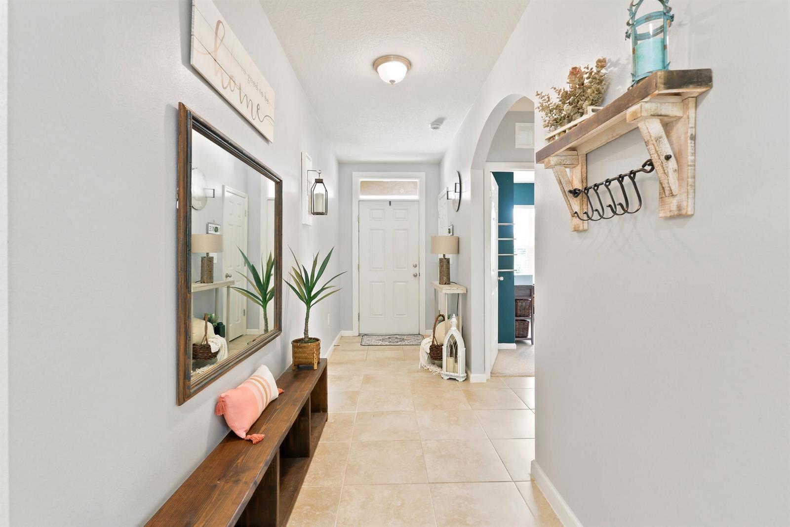 A bright entryway features tile flooring, a wooden bench, a mirror, and a wall shelf — 2096 SW Leafy Road, FL 34953, FL