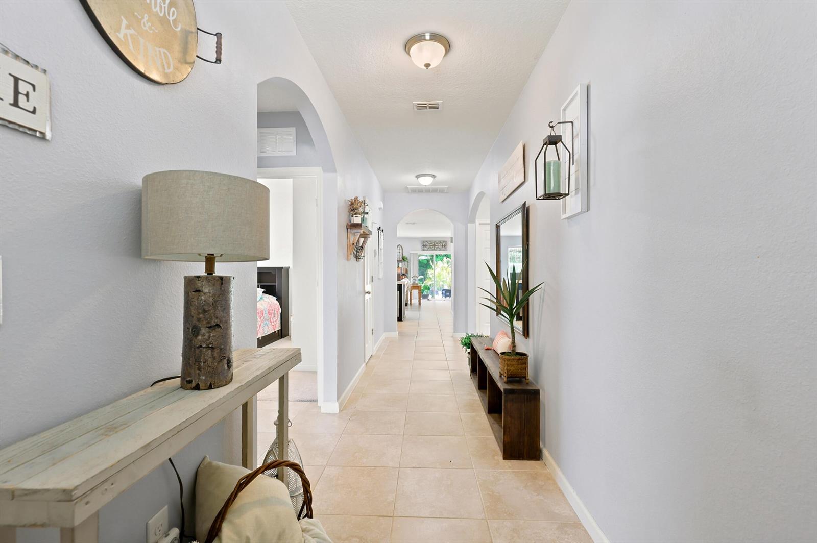A long hallway features light-colored tile flooring, arched doorways, and decorative wall decor — 2096 SW Leafy Road, FL 34953, FL