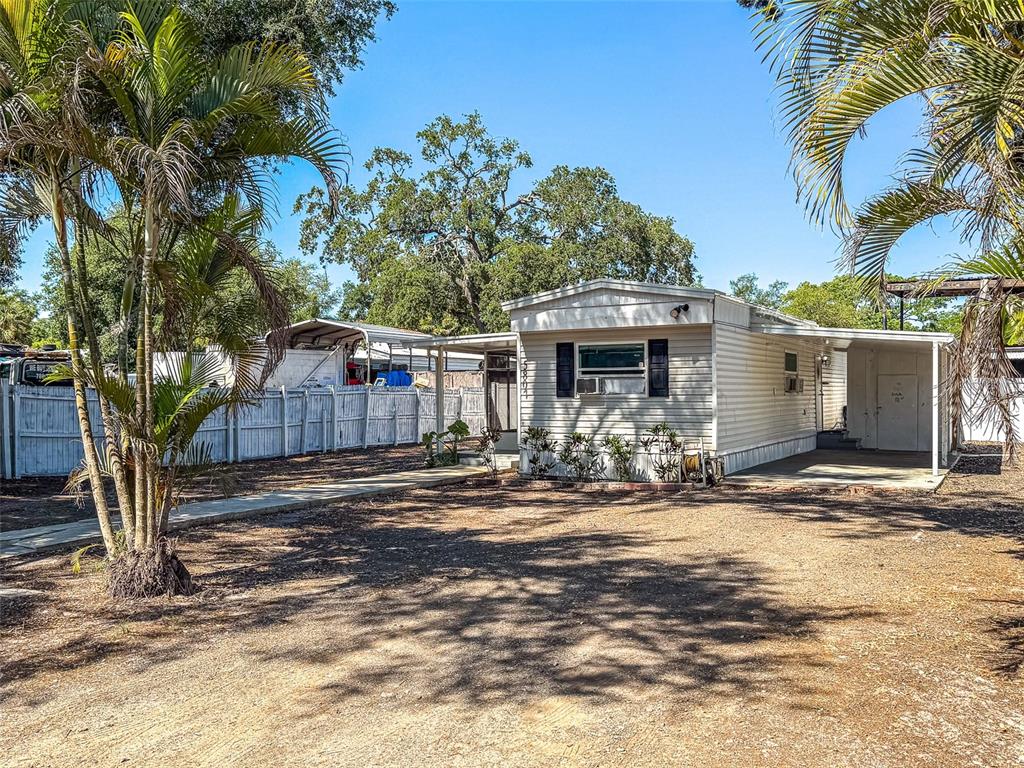 A single-story mobile home with a carport and a white fence sits on a dirt lot — 5807 BARRY LANE, TAMPA, FL