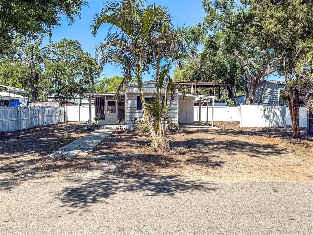 A single-story mobile home with a palm tree in the front yard and white fencing — 5807 BARRY LANE, TAMPA, FL