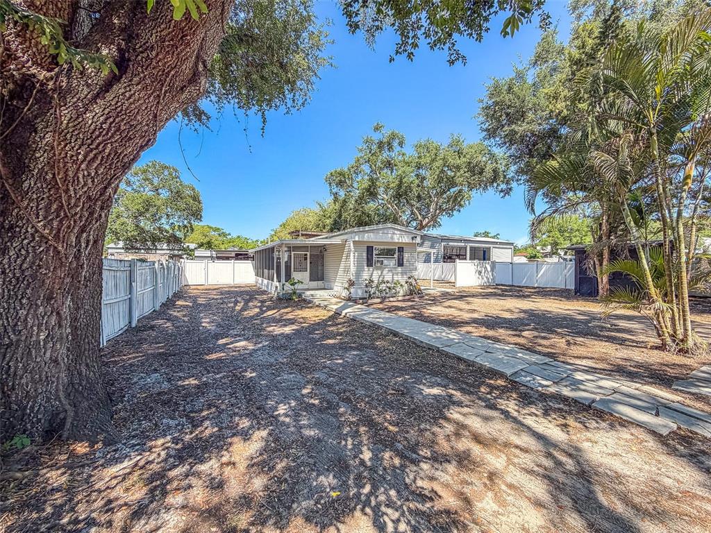 A single-story mobile home sits on a dirt lot with a large tree and fence — 5807 BARRY LANE, TAMPA, FL