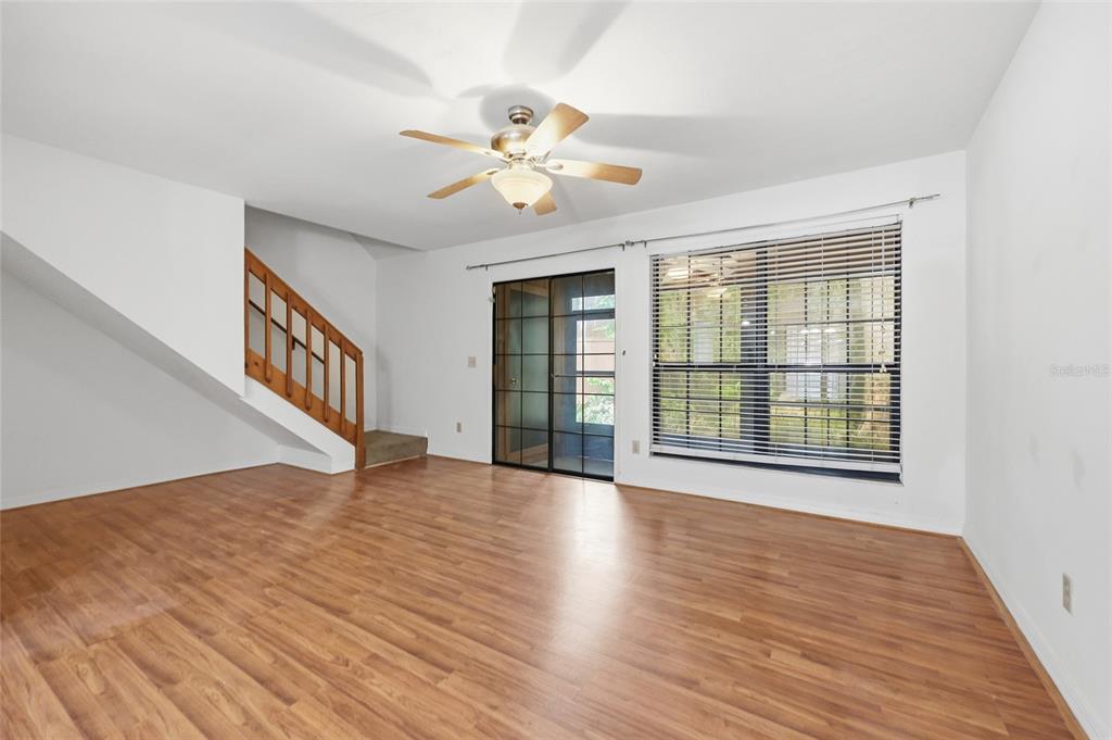 An empty living room features wood-look flooring, a ceiling fan, a staircase, and sliding doors — 852 SW 58TH TERRACE, GAINESVILLE, FL