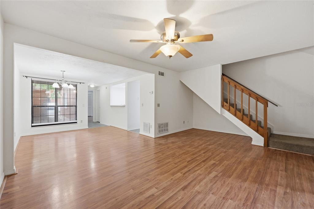 An open living room features wood-look flooring, a ceiling fan, and a wooden staircase — 852 SW 58TH TERRACE, GAINESVILLE, FL
