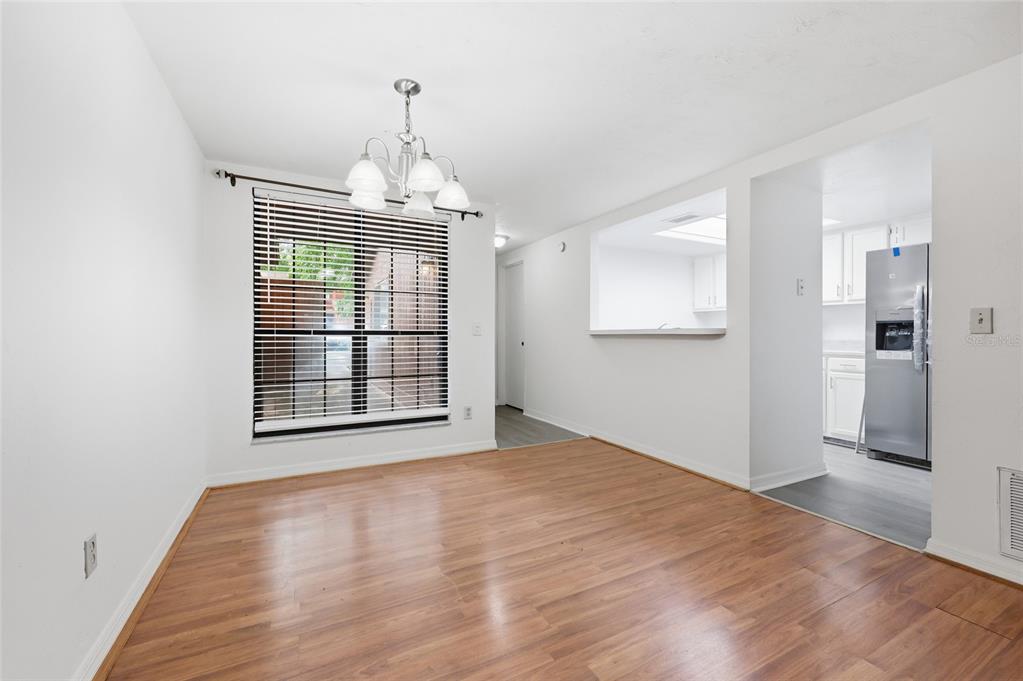 A dining area with wood-look flooring, a chandelier, and a pass-through window to the kitchen — 852 SW 58TH TERRACE, GAINESVILLE, FL
