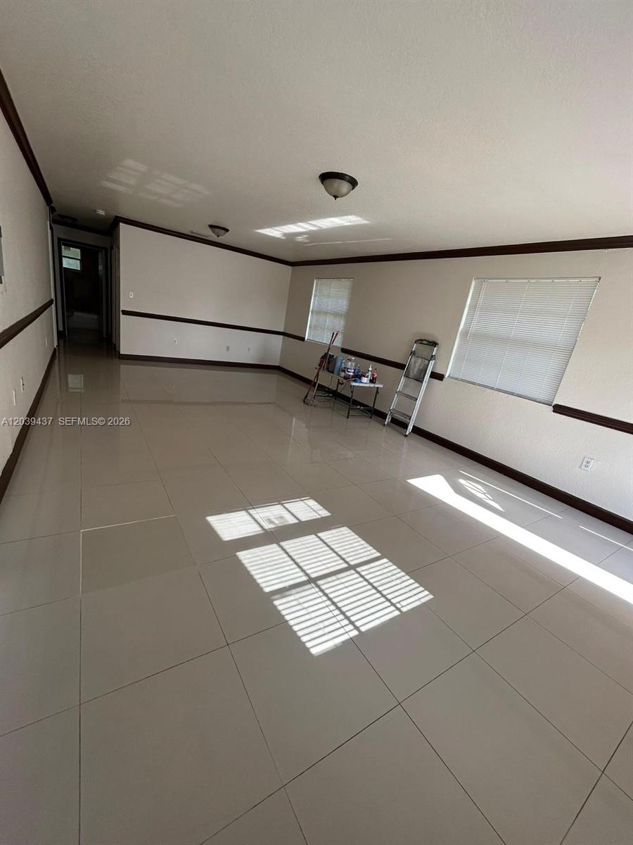 An empty room features light-colored tile flooring, beige walls with dark trim, and two windows — 1255 NW 55th Ter # 1257, Miami FL 33142, MIAMI, FL