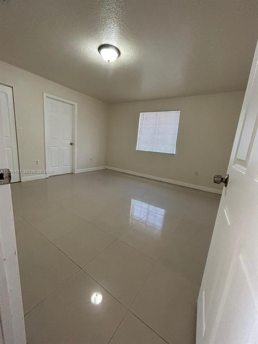 An empty room features light-colored tile flooring, white walls, and a single window with blinds — 1255 NW 55th Ter # 1257, Miami FL 33142, MIAMI, FL