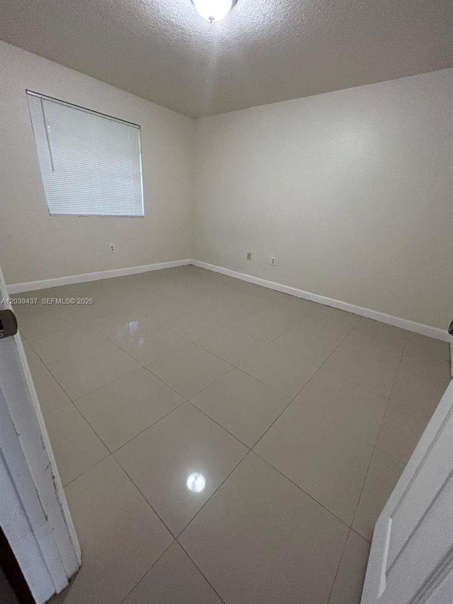 An empty bedroom features light-colored tile flooring, beige walls, and a single window — 1255 NW 55th Ter # 1257, Miami FL 33142, MIAMI, FL
