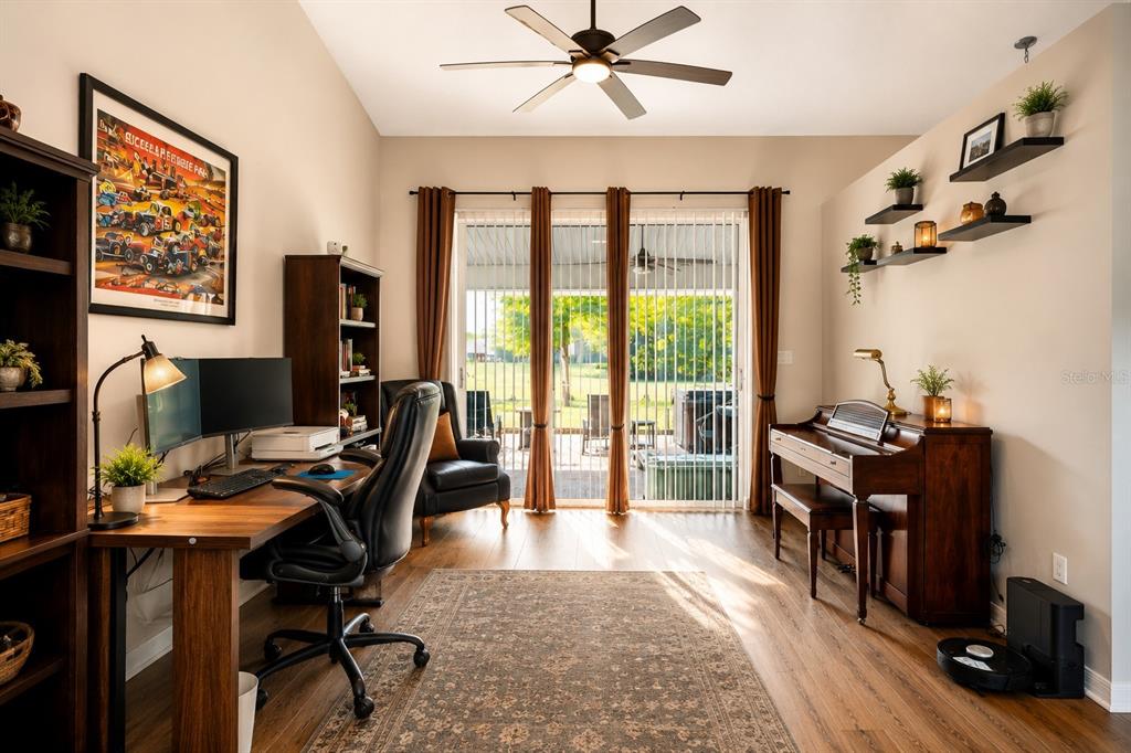 A home office features a desk, piano, shelving, and sliding glass doors leading to a patio — 25073 RIVERWALK DRIVE, LEESBURG, FL