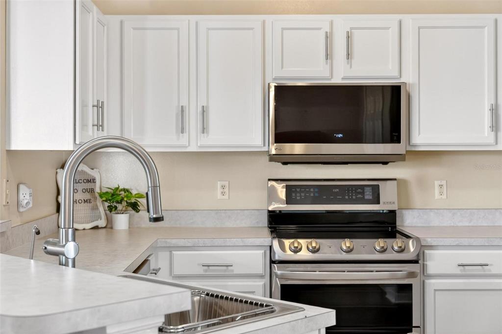 A kitchen features white cabinets, stainless steel appliances, and a light-colored countertop — 25073 RIVERWALK DRIVE, LEESBURG, FL