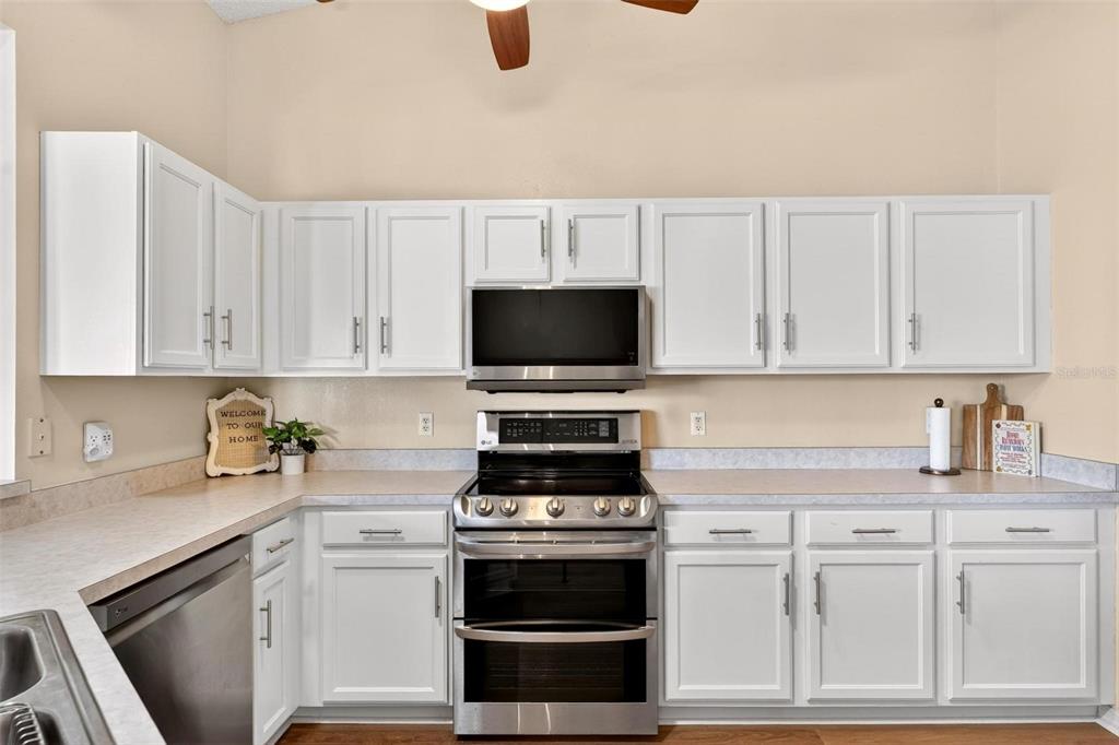 A kitchen features white cabinets, stainless steel appliances, and light-colored laminate countertops — 25073 RIVERWALK DRIVE, LEESBURG, FL