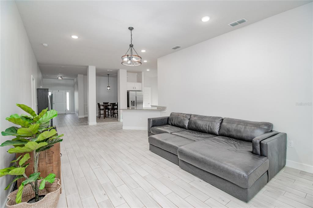 A living room with light tile flooring, a dark gray sectional sofa, and an open kitchen — 4820 SUMMIT VIEW WAY, AUBURNDALE, FL