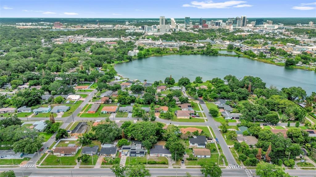 An aerial view shows a residential neighborhood bordering a lake with a city skyline beyond — 417 N TAMPA AVENUE, ORLANDO, FL