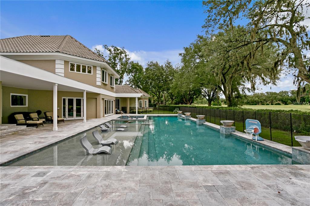 A swimming pool with a tanning ledge and lounge chairs sits behind a two-story house — 16601 AVILA BOULEVARD, TAMPA, FL