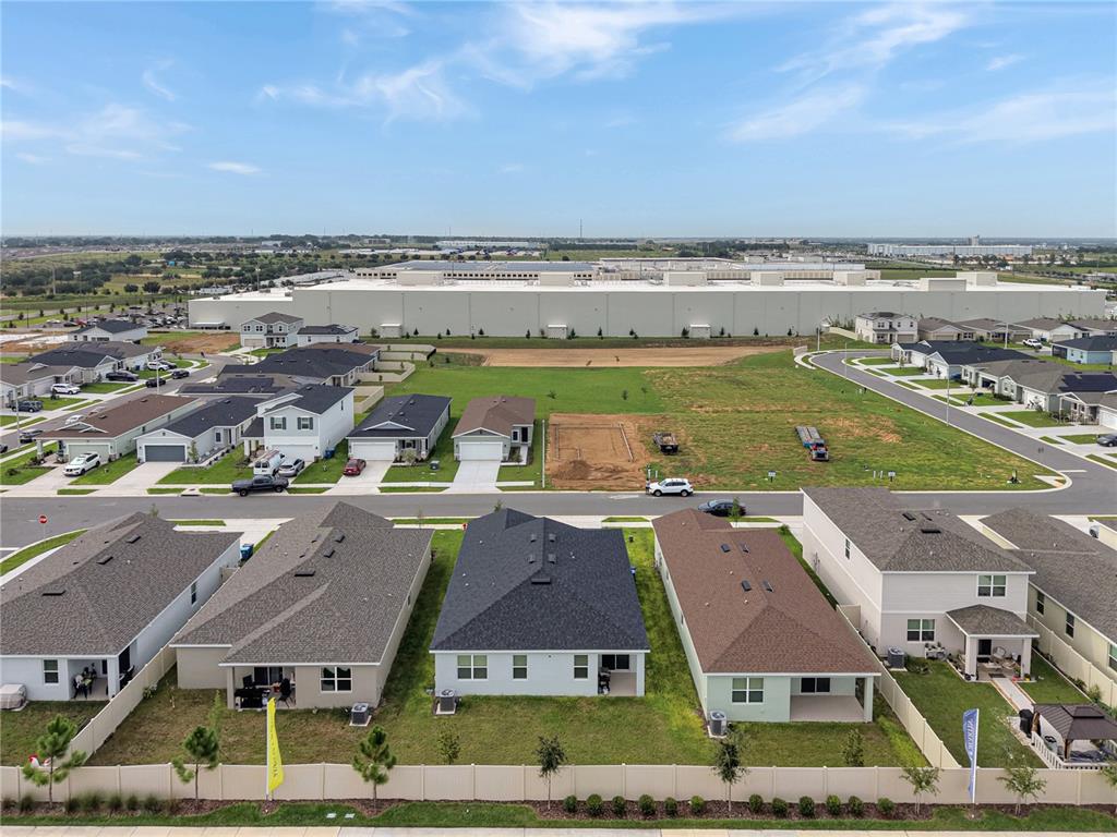 An aerial view shows a suburban neighborhood with new houses and a large warehouse nearby — 4136 LAVENDER COURT, LAKE HAMILTON, FL