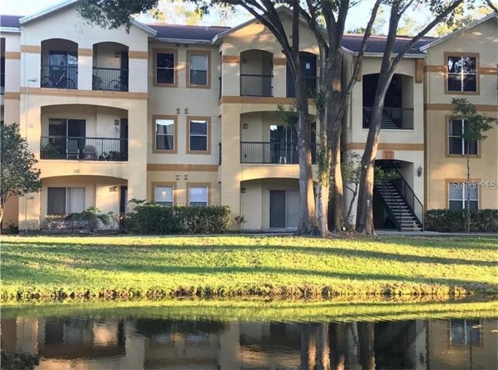 A three-story apartment building with balconies and a pond in the foreground — 5602 PINNACLE HEIGHTS CIRCLE UNIT 111, TAMPA, FL