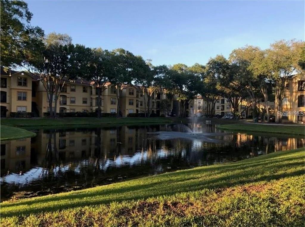 A pond with a fountain sits in front of multi-story apartment buildings and trees — 5602 PINNACLE HEIGHTS CIRCLE UNIT 111, TAMPA, FL