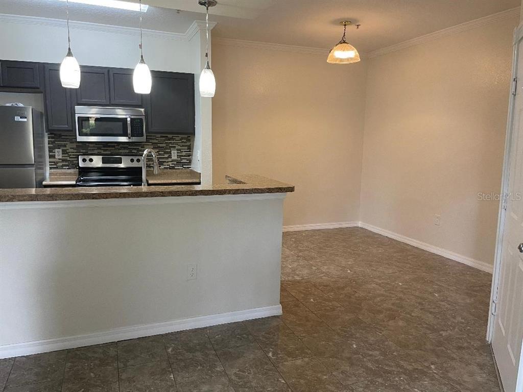 A kitchen with dark cabinets and stainless steel appliances overlooks an open dining area — 5602 PINNACLE HEIGHTS CIRCLE UNIT 111, TAMPA, FL