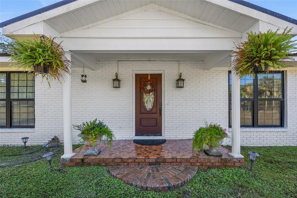 The front exterior of a white brick house features a covered porch with a brown door — 172 SW BRADSHAW GLEN, LAKE CITY, FL