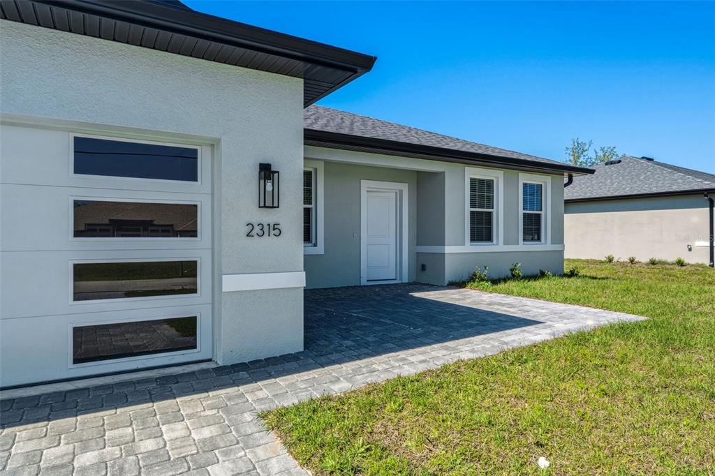 The exterior of a light-colored house features a paved walkway, a garage, and a door — 2315 MISTLETO LANE, NORTH PORT, FL