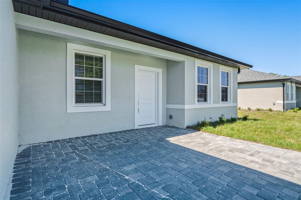 A paved patio sits before a light-colored house exterior with a white door and windows — 2315 MISTLETO LANE, NORTH PORT, FL