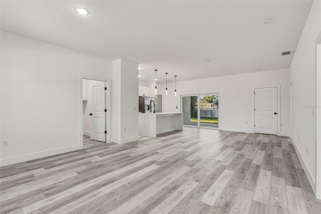 An open-concept living area features light gray wood-look flooring, white walls, and a kitchen island — 2315 MISTLETO LANE, NORTH PORT, FL