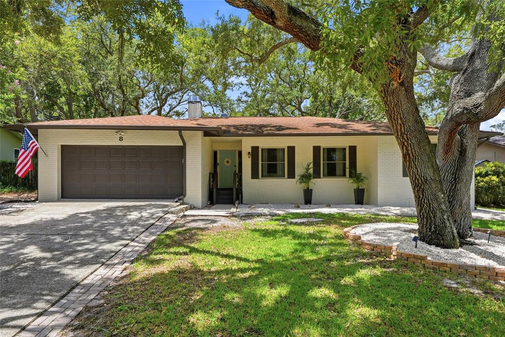 A single-story brick house with a two-car garage, a light green door, and large trees — 8 CLEARVIEW DRIVE, SAFETY HARBOR, FL