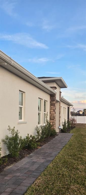 A side view of a beige stucco house with a stone pillar and paver walkway — 4244 ST THOMAS WAY, KISSIMMEE, FL