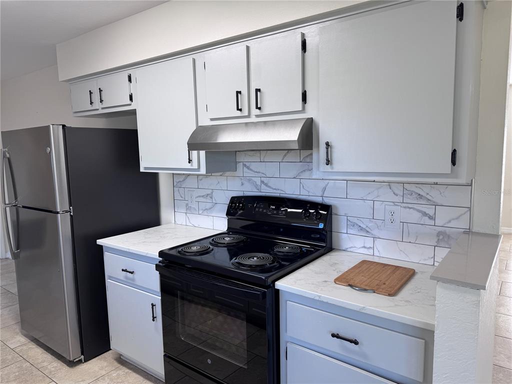 A kitchen features white cabinets, marble-patterned countertops, a subway tile backsplash, and black appliances — 15144 SW 27TH COURT, OCALA, FL