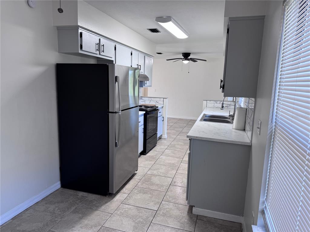 A kitchen features stainless steel appliances, gray cabinets, white countertops, and light-colored tile flooring — 15144 SW 27TH COURT, OCALA, FL