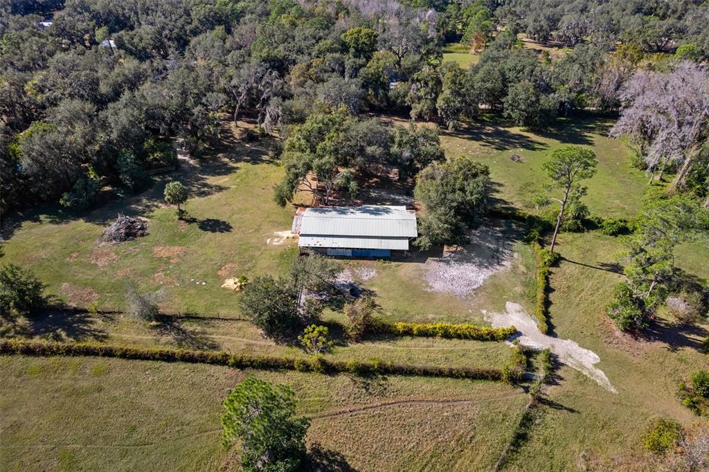 An aerial view shows a metal-roofed barn situated in a large, tree-lined grassy field — 27910 & 27750 DEBBIE ROAD, OKAHUMPKA, FL