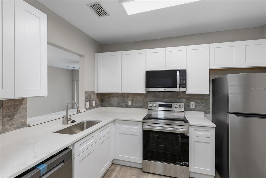 A kitchen features white cabinets, stainless steel appliances, and light countertops with a stone backsplash — 522 VILLA DEL SOL CIRCLE UNIT 201, ORLANDO, FL