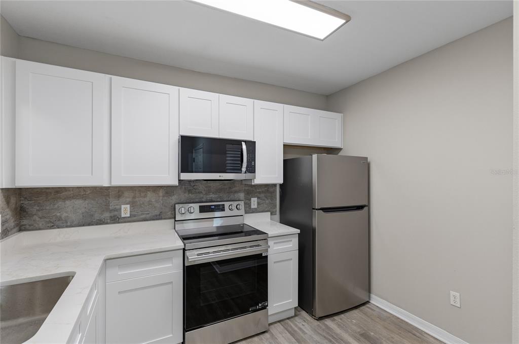 A kitchen features white cabinets, stainless steel appliances, a stone backsplash, and light-colored countertops — 522 VILLA DEL SOL CIRCLE UNIT 201, ORLANDO, FL