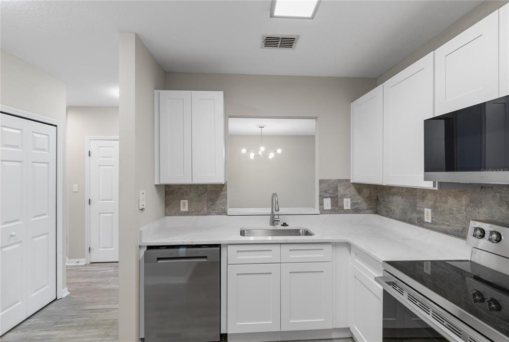 A kitchen features white cabinets, stainless steel appliances, a stone backsplash, and a pass-through window — 522 VILLA DEL SOL CIRCLE UNIT 201, ORLANDO, FL