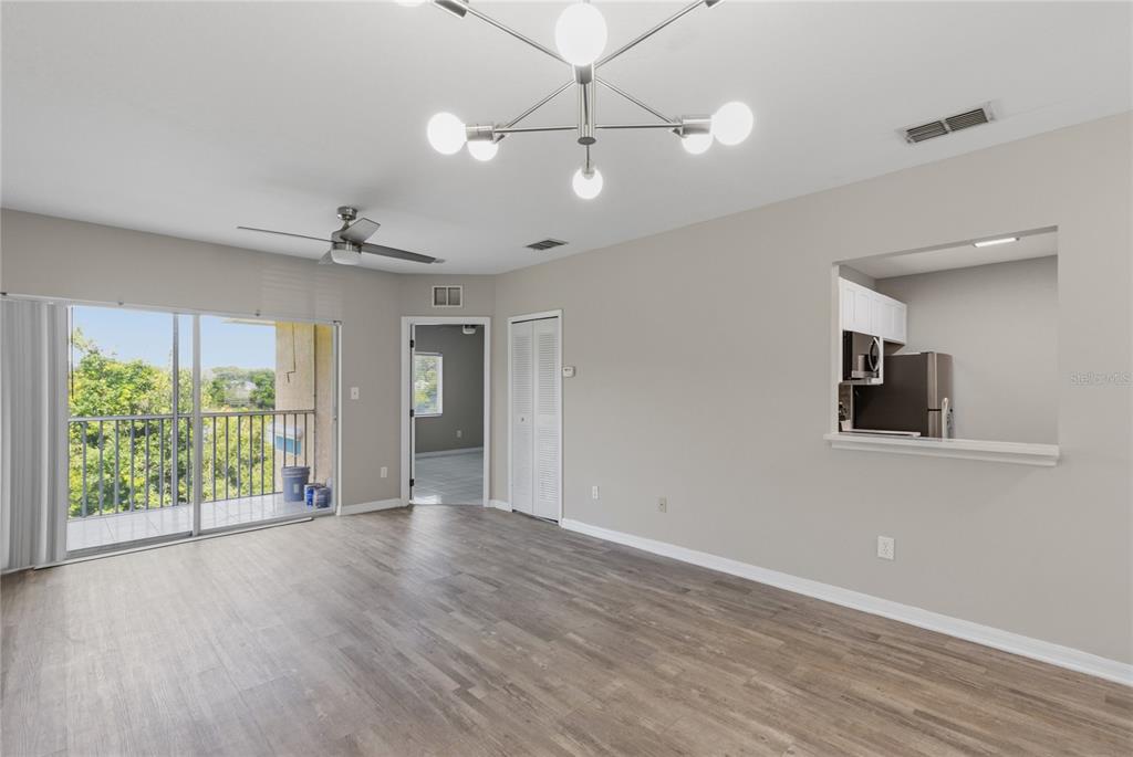 A living room with wood-look flooring, a ceiling fan, a chandelier, and a balcony view — 522 VILLA DEL SOL CIRCLE UNIT 201, ORLANDO, FL