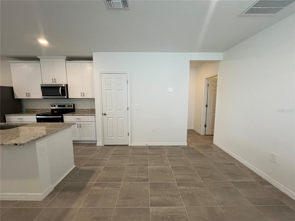 A kitchen with white cabinets, granite countertops, and tile flooring opens to a hallway — 4973 KAIA AVENUE, WINTER HAVEN, FL