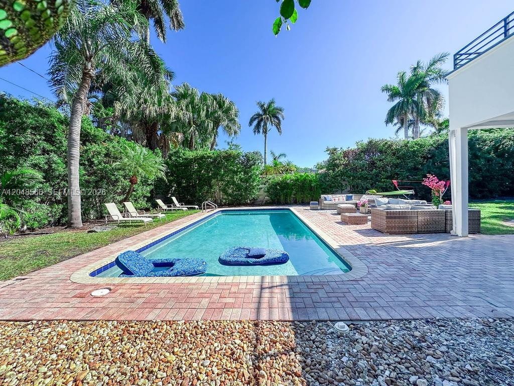 A rectangular swimming pool sits on a brick patio surrounded by palm trees and landscaping — 1255 Jackson St, Hollywood FL 33019, HOLLYWOOD, FL