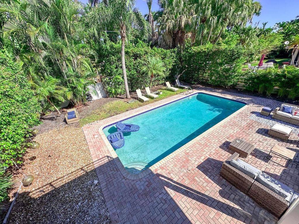 An outdoor swimming pool with a brick patio and lounge chairs surrounded by lush greenery — 1255 Jackson St, Hollywood FL 33019, HOLLYWOOD, FL