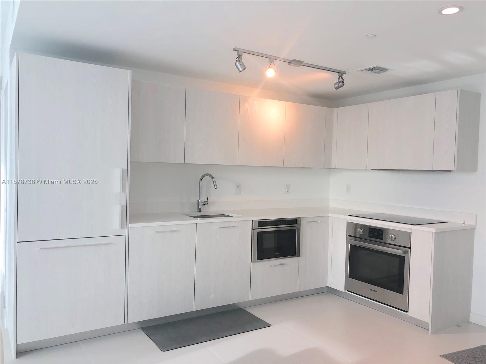 A modern kitchen features light wood cabinetry, stainless steel appliances, and white tile flooring — 501 NE 31 street # 1709, Miami FL 33137, MIAMI, FL