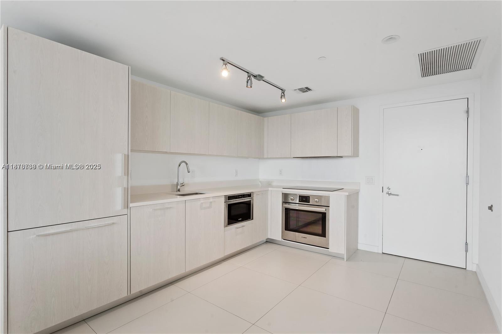 A modern kitchen features light wood cabinetry, white countertops, a built-in oven, and a sink — 501 NE 31 street # 1709, Miami FL 33137, MIAMI, FL