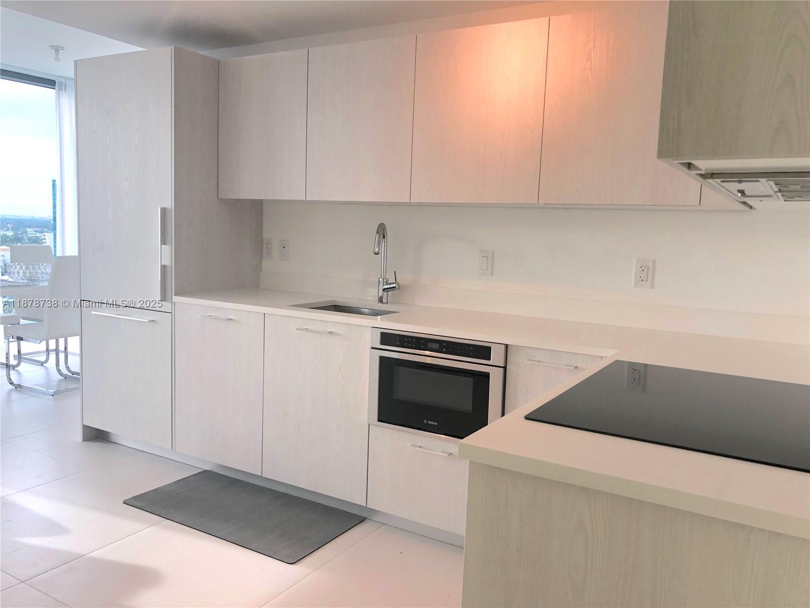 A modern kitchen features light wood cabinetry, stainless steel appliances, and white tile flooring — 501 NE 31 street # 1709, Miami FL 33137, MIAMI, FL